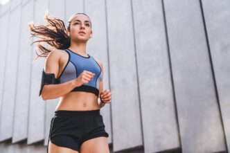 A female runner jogging outside with her hair blowing back, wearing earbuds and workout clothes.