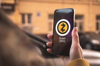 Hand holding a smartphone displaying the Zcash (ZEC) cryptocurrency logo and ticker on its screen.