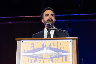 Mayoral candidate Zohran Mamdani speaks at a podium with a sign that reads "NEW YORK IS NOT FOR SALE."