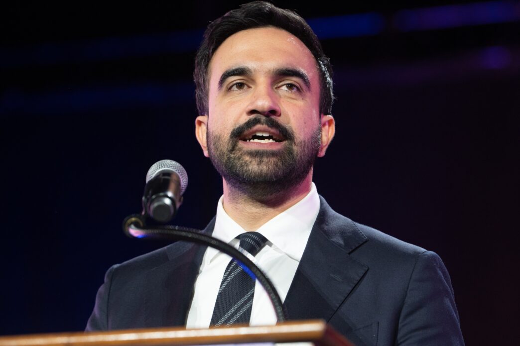 Close-up of mayoral candidate Zohran Mamdani speaking at a microphone on a stage.