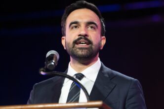 Close-up of mayoral candidate Zohran Mamdani speaking at a microphone on a stage.