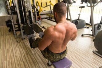 A person performs a heavy weight exercise, likely a back exercise, in a gym setting.