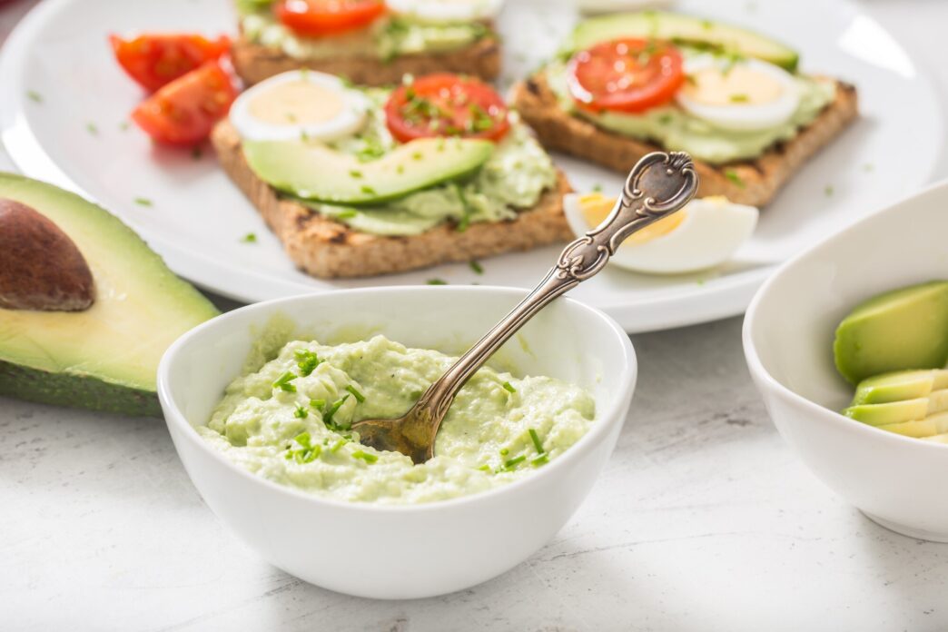 Overhead shot of avocado toast topped with a fried egg, diced tomato, and chives.