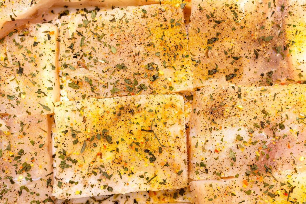 Top-down view of a background made of square pieces of cod fillet, seasoned with spices.