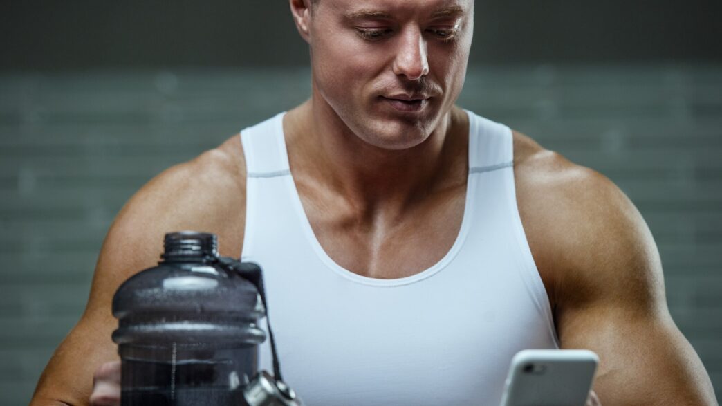 A bodybuilder drinks water from a bottle after a workout.