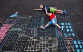 A chalk drawing on asphalt depicts a boy flying over a cityscape and saving a human superhero.