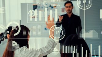 Businesspeople seated around a table in a meeting, with a graphic displayed on a screen.
