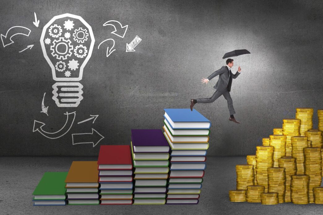 A businessman jumps while holding an umbrella against steps made of books in front of a lightbulb drawing.