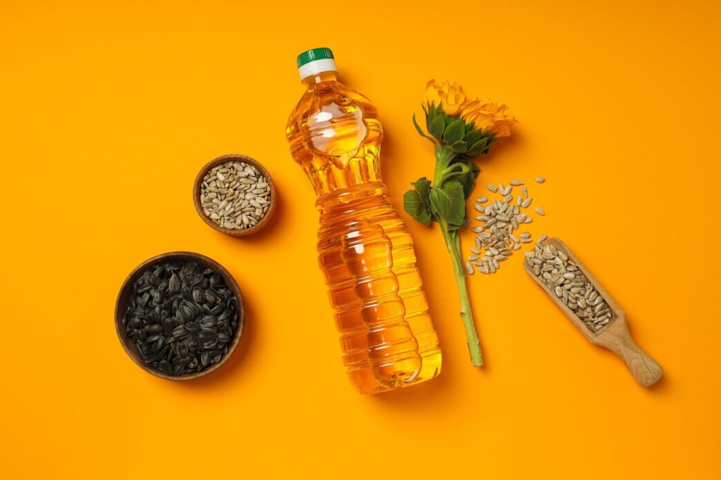 Close-up of a glass bottle of sunflower oil with various cooking ingredients arranged around it, such as garlic, herbs, and spices.