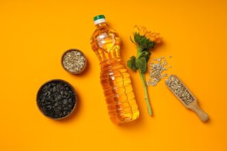 Close-up of a glass bottle of sunflower oil with various cooking ingredients arranged around it, such as garlic, herbs, and spices.