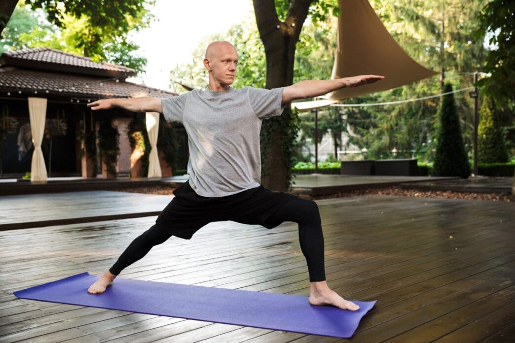 A young man in athletic wear stretches on a yoga mat outdoors.