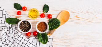 Assortment of colorful spices, fresh vegetables, and herbs arranged on a white wooden background, likely for cooking.