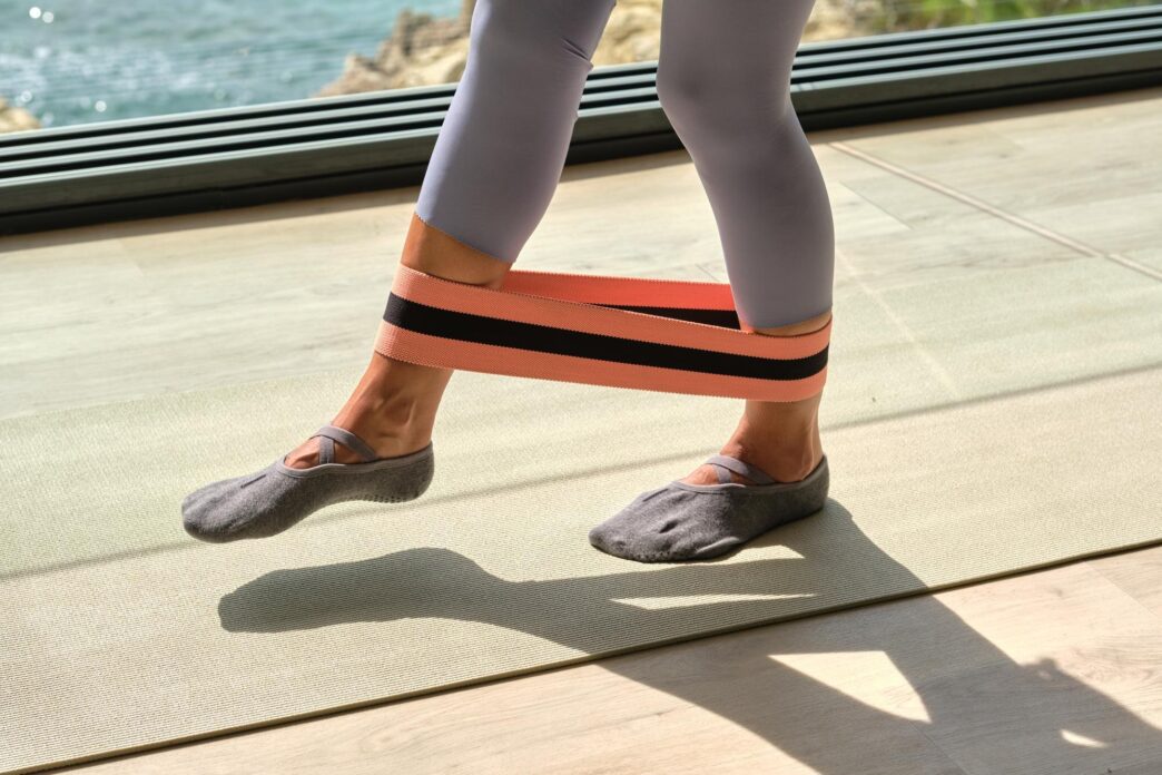 Unrecognizable sportswoman in activewear exercises with a resistance band in a bright studio.
