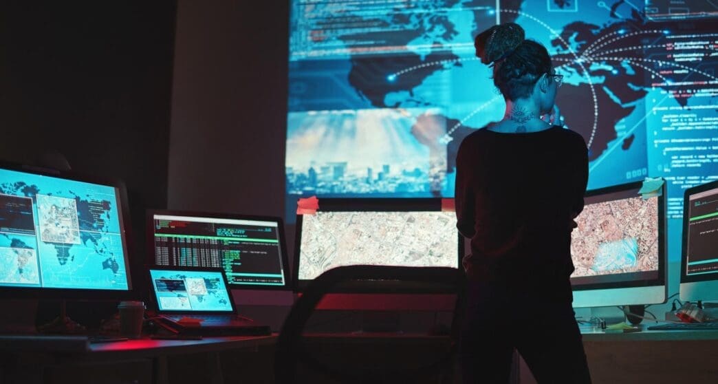 A woman in a dark room interacts with a digital map of a global network, likely investigating cybersecurity threats like phishing and ransomware.