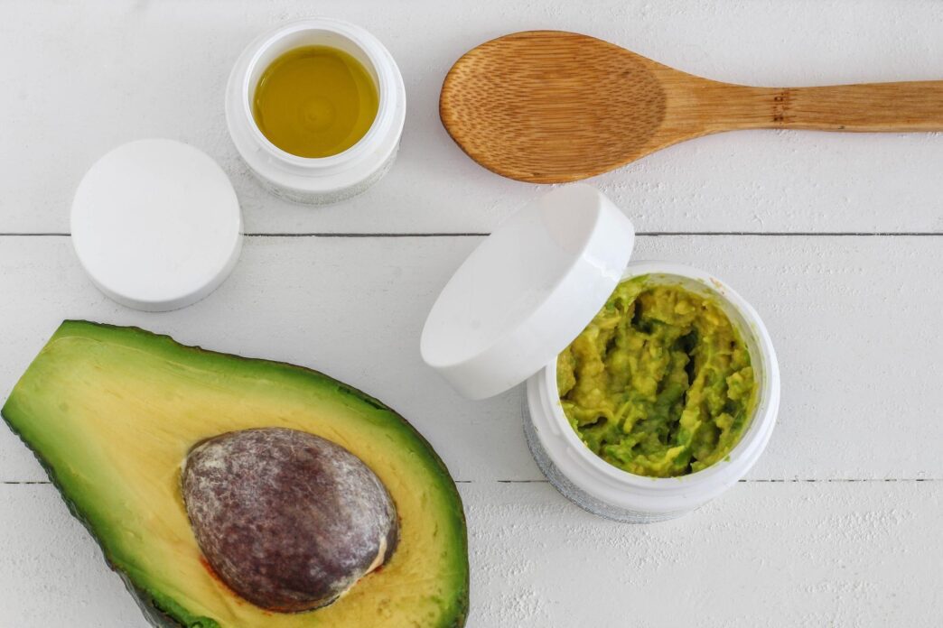 Overhead view of an avocado half and a small bottle of oil on a table.