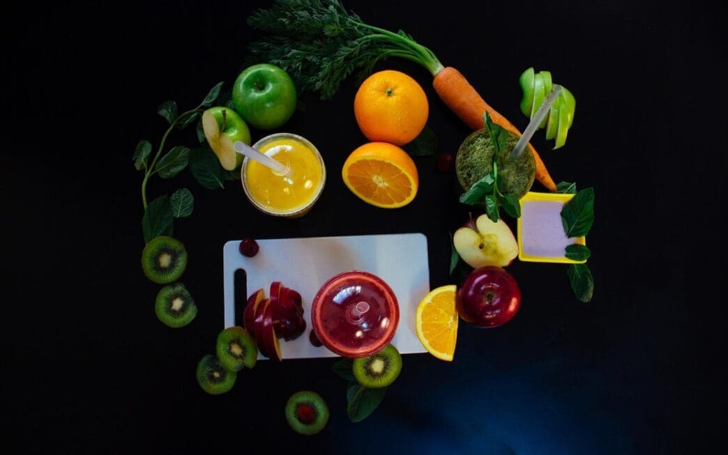Overhead view of various fruits and a glass of juice arranged on a black surface.