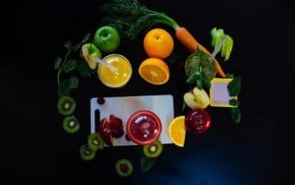 Overhead view of various fruits and a glass of juice arranged on a black surface.