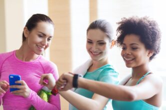 A woman in a gym smiles while looking at her wristwatch.