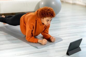 A young, fit African woman in workout clothes performs a plank exercise on a yoga mat.