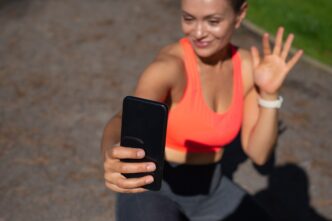 Smiling woman holding a black smartphone while sitting on a running track.