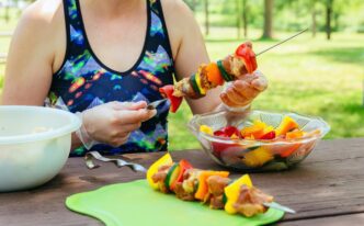 Grilled pork barbecue skewers and assorted vegetables rest on a wooden cutting board.