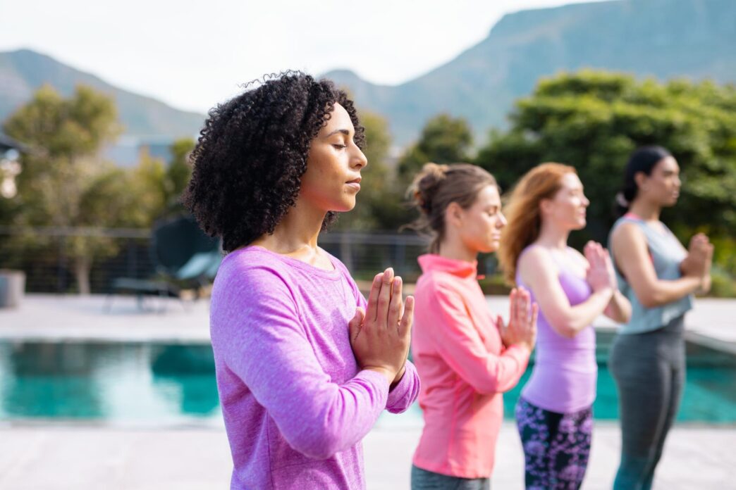Happy group of diverse friends in athletic wear practicing yoga and meditating outdoors in a garden.