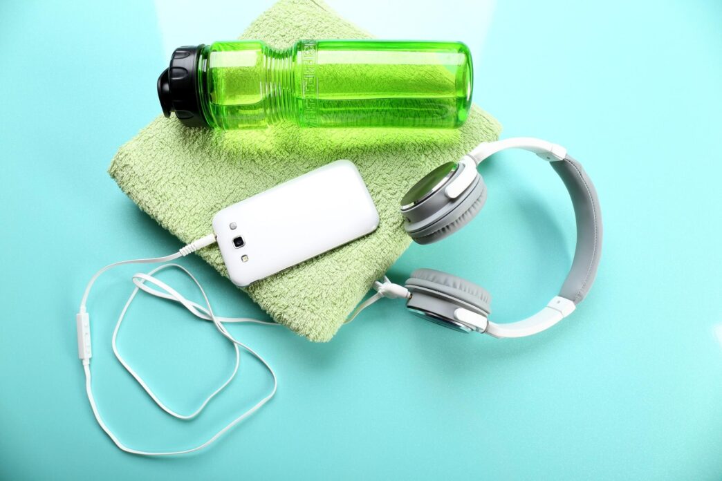 Headphones and various sports equipment, such as a water bottle and sneakers, are arranged on a light blue surface.