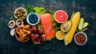 Overhead shot of a rustic wooden table displaying an assortment of fresh fish, nuts, vegetables, and fruits, with space for text.