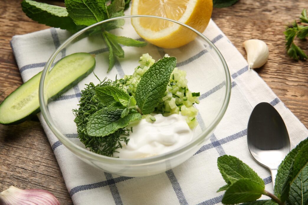 A wooden table holds a bowl of ingredients and a container for making yogurt sauce.