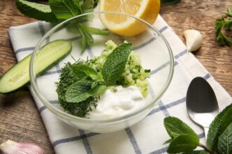 A wooden table holds a bowl of ingredients and a container for making yogurt sauce.