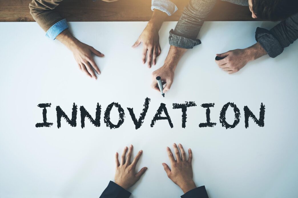 A diverse group of people collaborate around a surface with the word "innovation" on it, set against a plain white background.