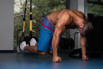 A Latin adult athlete performs push-ups using TRX straps as part of a bodybuilding workout.