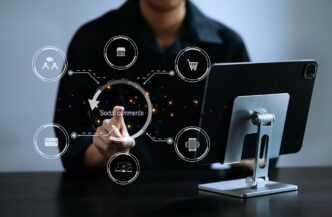 A man's hand uses a smartphone and tablet, displaying social commerce icons and illustrating social media marketing in an office setting.