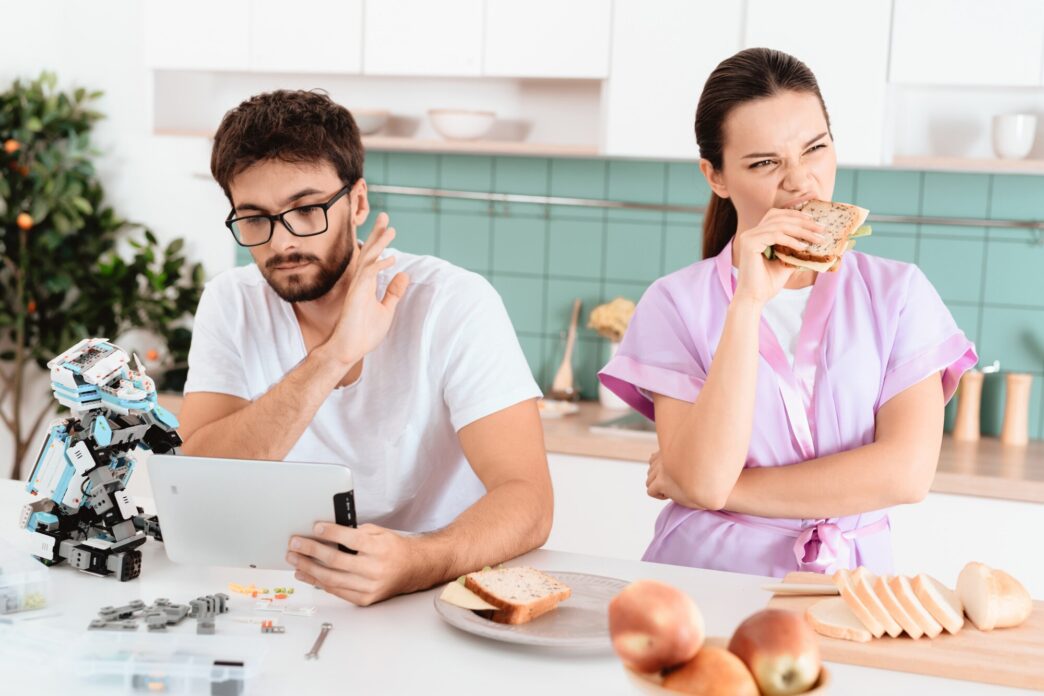 A man examines a small robot while reading a tablet.
