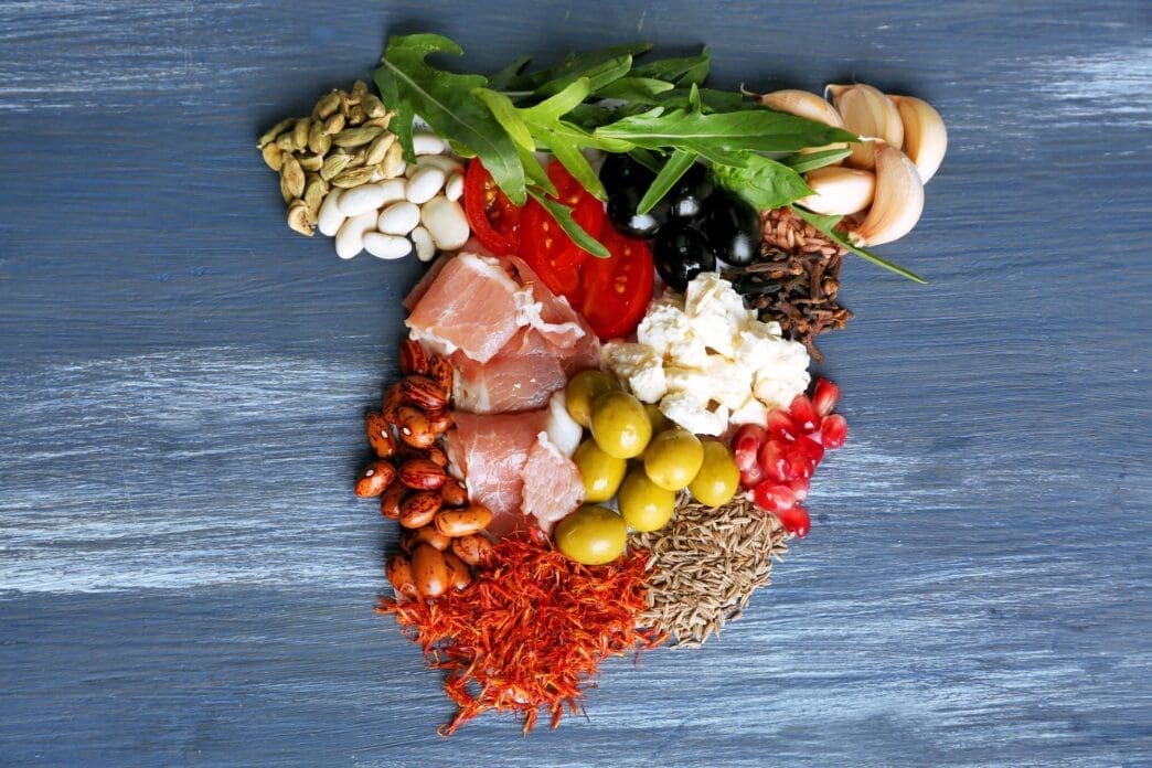 Map of Spain created with various food items like chorizo, olives, and tomatoes, arranged on a colorful wooden surface.