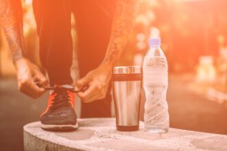 A person ties their shoelace next to a bottle and a mug.