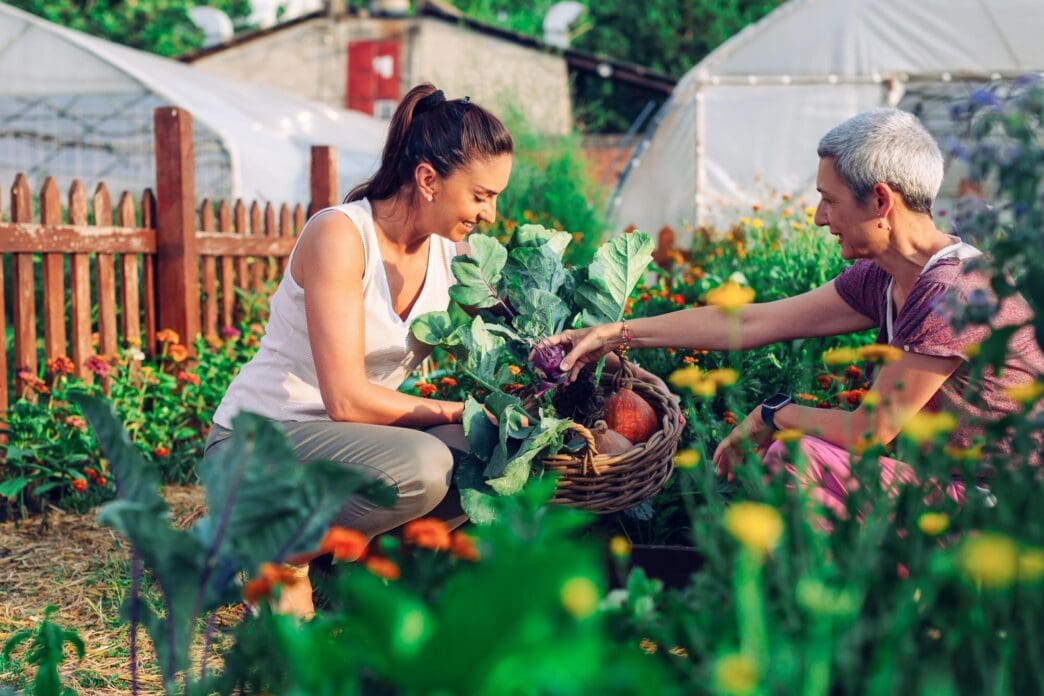 A mother and daughter are gardening together, with the daughter learning from her mother.