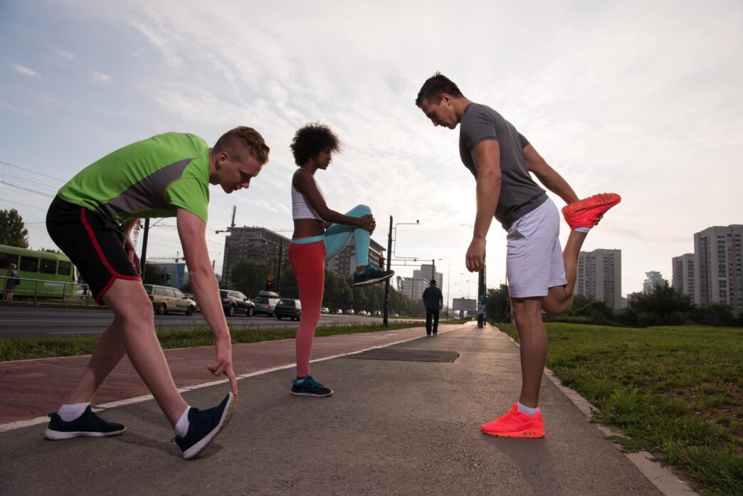 A diverse group of young people jogs together on a city street at sunrise.