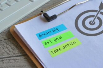 A paper clipboard displays a target icon, the words "DREAM BIG SET GOAL," and "TAKE ACTION," conveying a message of motivation.