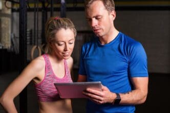 A personal trainer points to a workout plan while speaking to a woman.