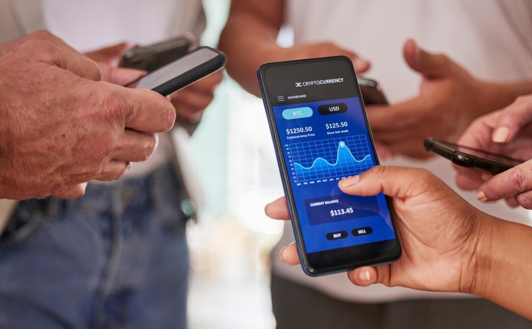 Hands interacting with a phone screen displaying cryptocurrency trading information, graphs, and financial data.