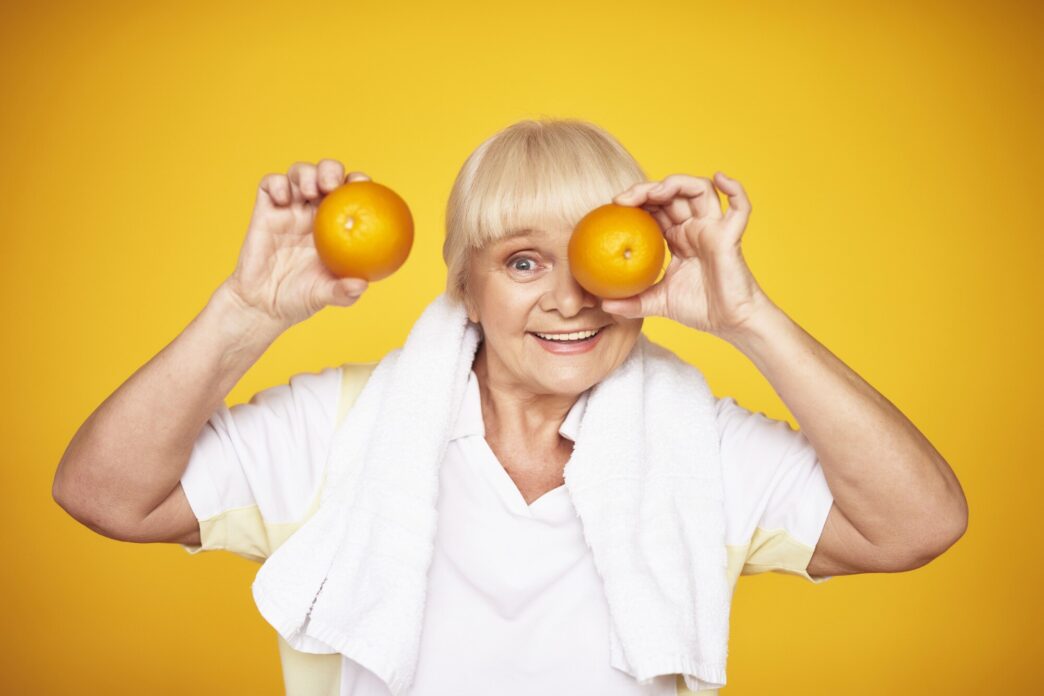 A smiling elderly woman holds oranges, representing the concept of vitamin C.