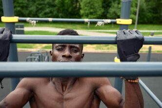 A Black man exercises outdoors in a park, using a chest machine.