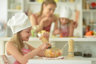 A young girl with a happy expression eats a salad in a kitchen.