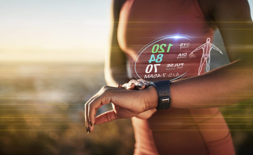 A black woman's hands hold a smartwatch displaying a 3D holographic overlay, suggesting fitness data during an outdoor workout.