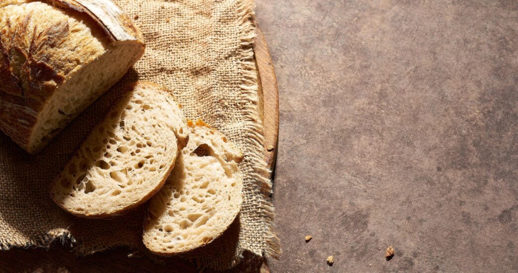 Sliced bread on a wooden board with crumbs on a painted surface.