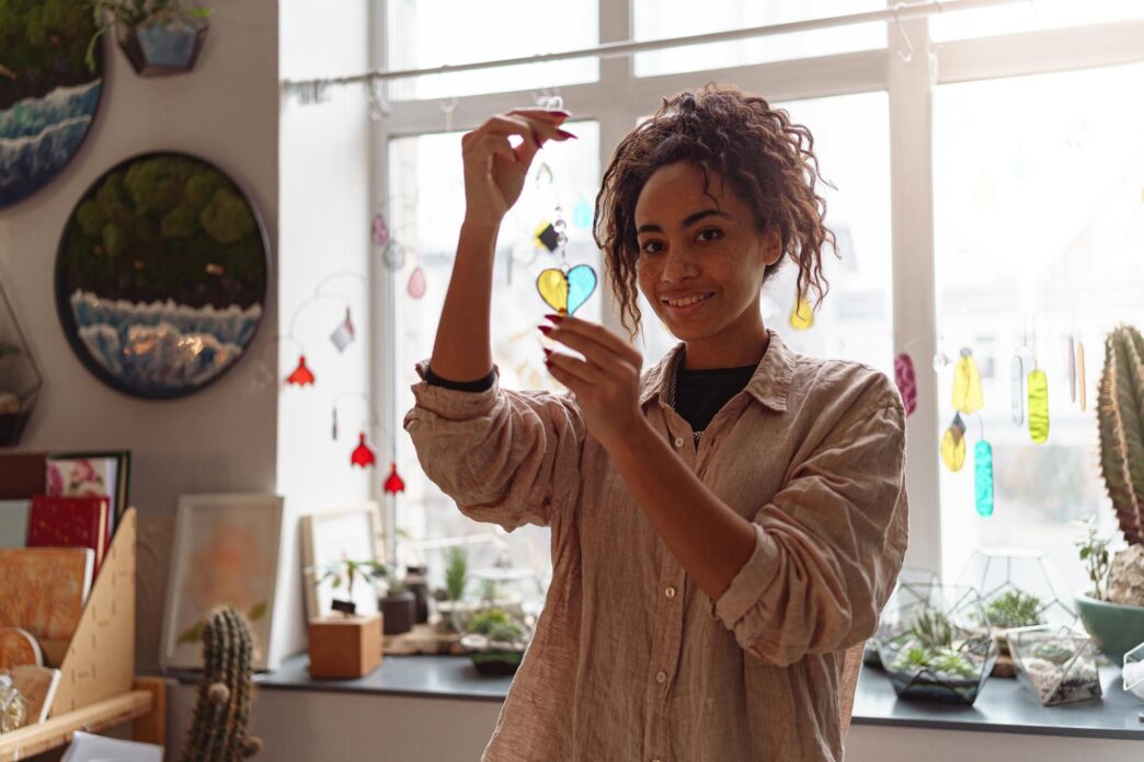 Smiling woman holding a heart-shaped glass decoration in a home decor studio.