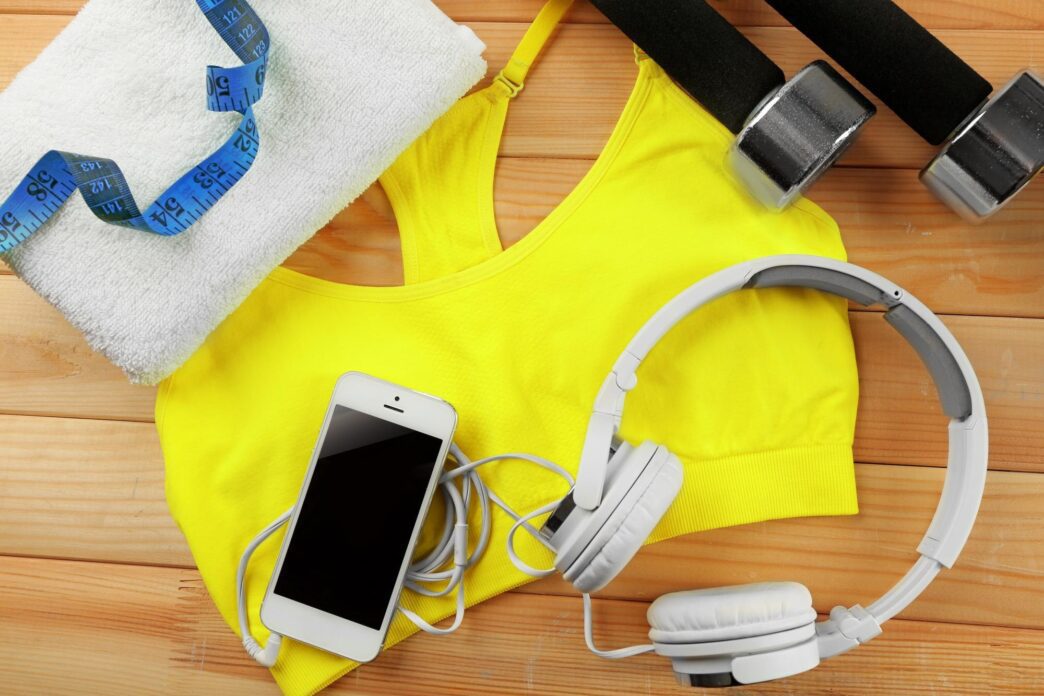 Assorted sports clothing and equipment, such as shoes and balls, are arranged on a wooden surface.