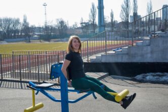 A young woman exercises her legs outdoors, using either a machine or dumbbells, promoting fitness and a healthy lifestyle.