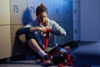 A sportswoman in a locker room wraps her wrist with a bandage, preparing for a boxing workout.